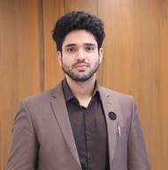 Portrait photo of Qutbuddin Habib, male with short hair, wearing a dark blazer and shirt, looking confident with folded arms